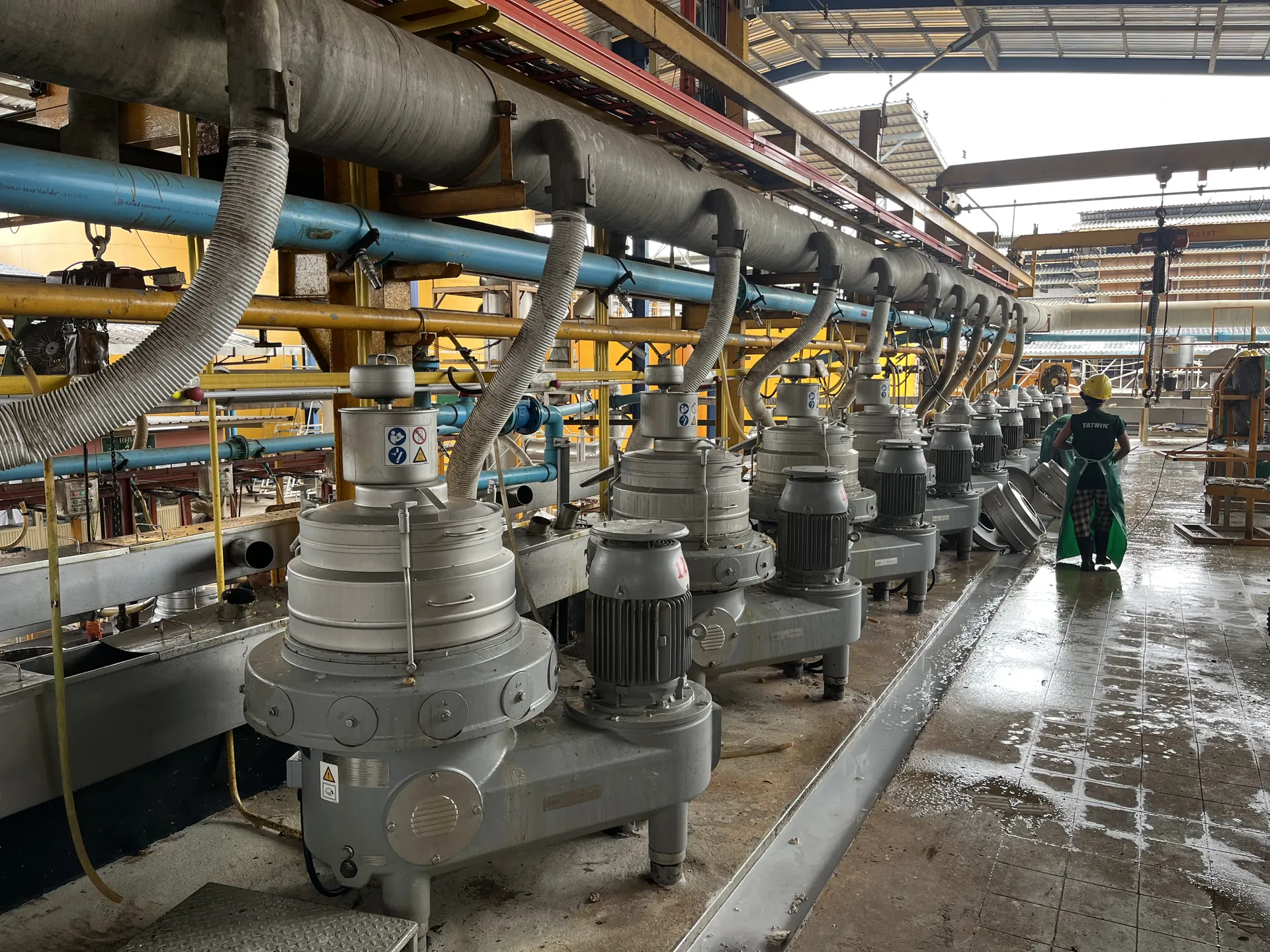 Long row of latex centrifuge separators with a worker walking the aisle